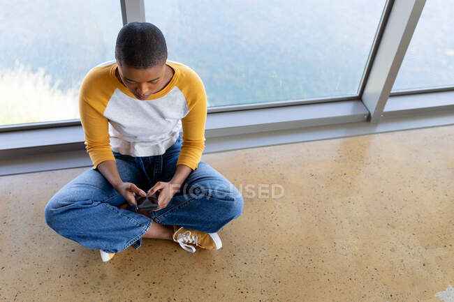 Messagerie texte femme d'affaires par smartphone tout en étant assis jambes croisées sur le sol dans le bureau. entreprise indépendante créative, technologie sans fil et bureau. — Photo de stock