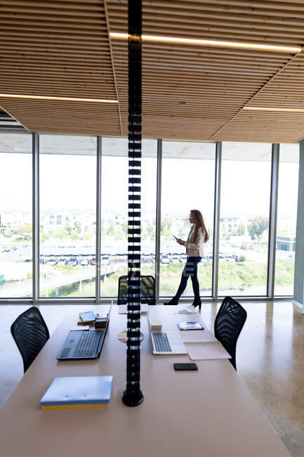 Vista lateral de empresária usando tablet digital enquanto se inclina na janela no escritório criativo. negócios, escritório local de trabalho e tecnologia sem fio. — Fotografia de Stock