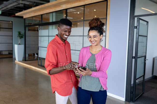 Cheerful young businesswoman showing smartphone to male colleague while standing in creative office. creative business, wireless technology and office workplace. — Stock Photo