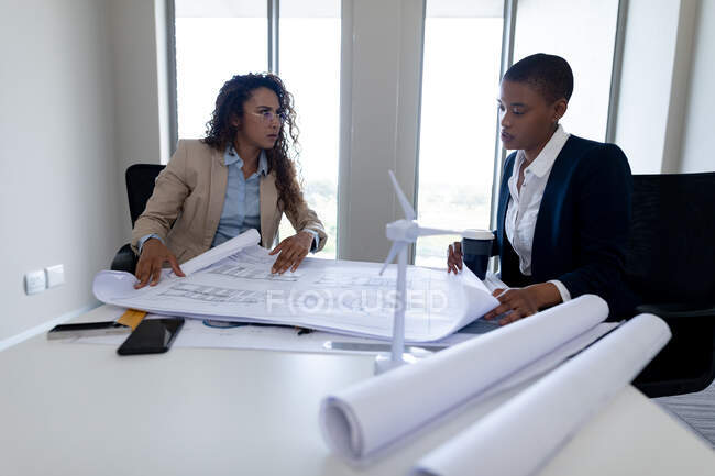 Multiracial female architects brainstorming over blueprint at desk in office. business, architect and creative office. — Stock Photo