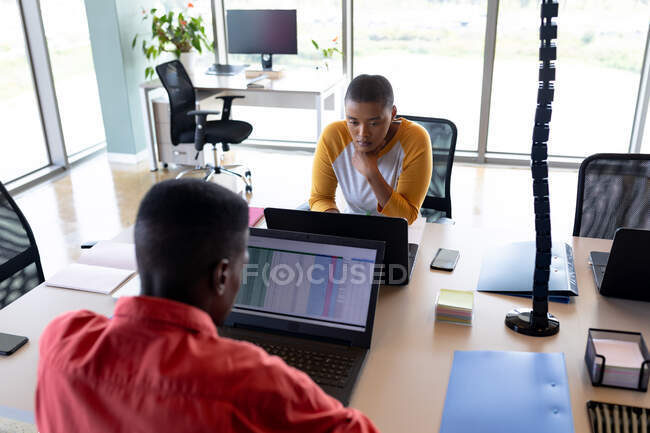 Mujer de negocios afroamericana y hombre de negocios que trabaja en computadoras portátiles en el escritorio en la oficina creativa. negocio creativo, tecnología inalámbrica y lugar de trabajo de oficina. - foto de stock