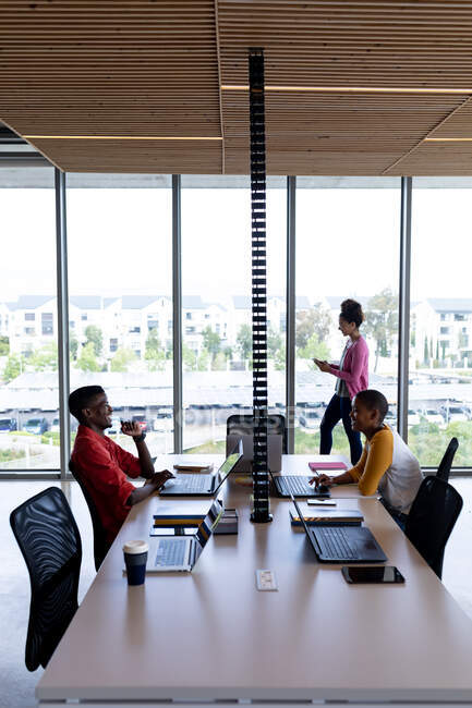 Colegas afro-americanos sorrindo enquanto trabalham em laptops na mesa no escritório criativo. negócio criativo, tecnologia sem fio e local de trabalho de escritório. — Fotografia de Stock