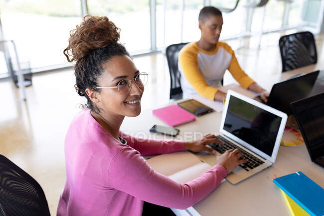 Портрет улыбающейся двуличной деловой женщины, работающей на ноутбуке с копировальным пространством в креативном кабинете. креативный бизнес, беспроводные технологии и офисное рабочее место — стоковое фото