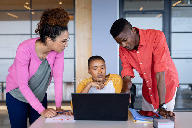 Multiracial male and female colleagues in casuals discussing over laptop in creative office. creative business, modern office and wireless technology. — Stock Photo