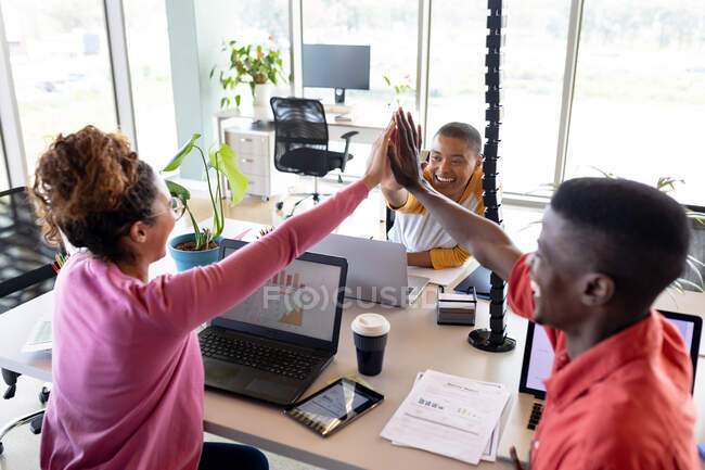 Cheerful multiracial business colleagues giving high-five at desk in creative office. creative business, modern office and wireless technology. — Stock Photo