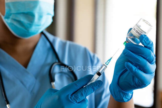 Doctora en mascarilla protectora llenando jeringa con vacuna en la clínica durante covid-19. servicios sanitarios, prevención de enfermedades y pandemia. - foto de stock