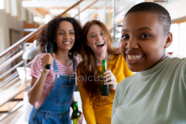 Femme heureuse prenant selfie avec des amies multiraciales tenant des bouteilles de bière à la maison. amitié, socialisation et loisirs à la maison. — Photo de stock