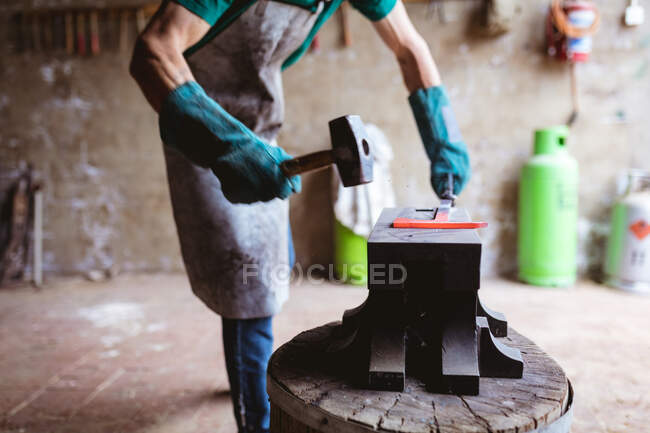 Midsection of blacksmith in protective gloves forging with hammer on anvil in industry. forging, metalwork and manufacturing industry. — Stock Photo