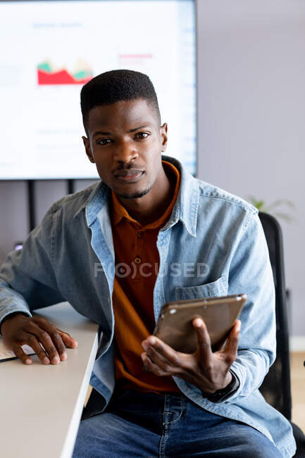 Ritratto di sicuro uomo d'affari africano in casuali con tablet digitale seduto in carica. business creativo, ufficio moderno e tecnologia wireless. — Foto stock