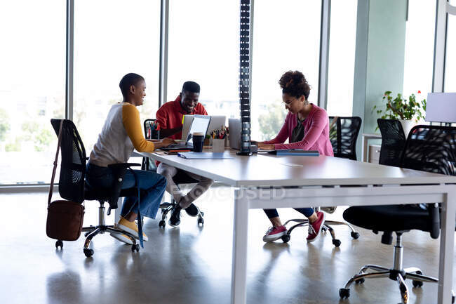 Des collègues d'affaires multiraciaux dans des occasionnels souriant tout en travaillant sur des ordinateurs portables dans un bureau créatif. entreprise créative, bureau moderne et technologie sans fil. — Photo de stock