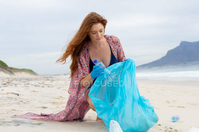 Kaukasische junge Frau in Freizeitanzügen sammelt Plastikmüll in Tüten am Strand. Umweltsanierung, Plastikverschmutzung und Verantwortung. — Stockfoto