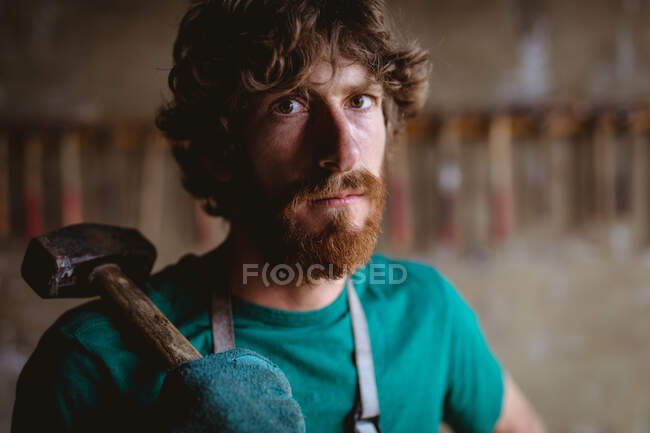 Portrait of confident bearded blacksmith holding hammer in manufacturing industry. forging, metalwork and manufacturing industry. — Stock Photo