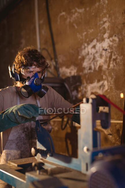 Herrero con máscara de gas usando maquinaria mientras trabaja en la industria manufacturera. forja, metalurgia e industria manufacturera. - foto de stock