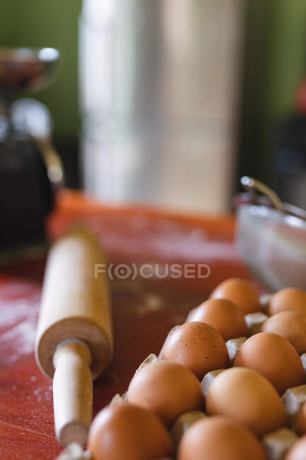Close-up of brown eggs on carton by rolling pin on wooden table at home. organic and healthy eating. — Stock Photo