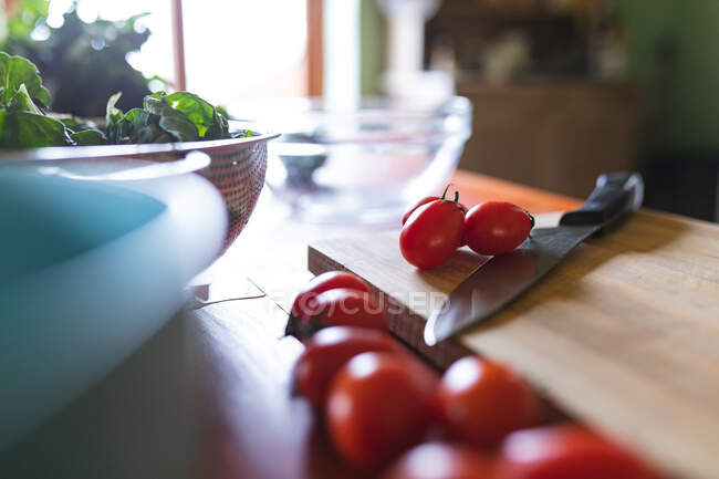 Close-up of fresh red cherry tomatoes with knife on wooden cutting board in kitchen. organic and healthy eating. — Stock Photo