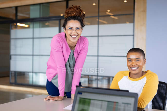 Retrato de mujeres de negocios multirraciales sonrientes en casuales en el escritorio en la oficina creativa. negocios creativos y negocios modernos. - foto de stock