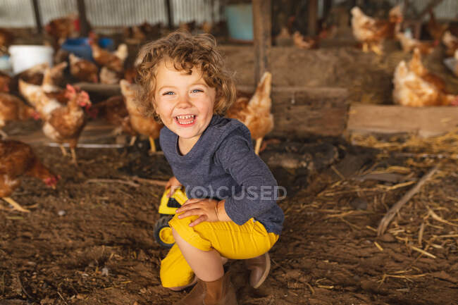 Retrato de niño lindo feliz arrodillado con gallinas en el fondo en la granja avícola. la infancia, la granja y la avicultura. - foto de stock