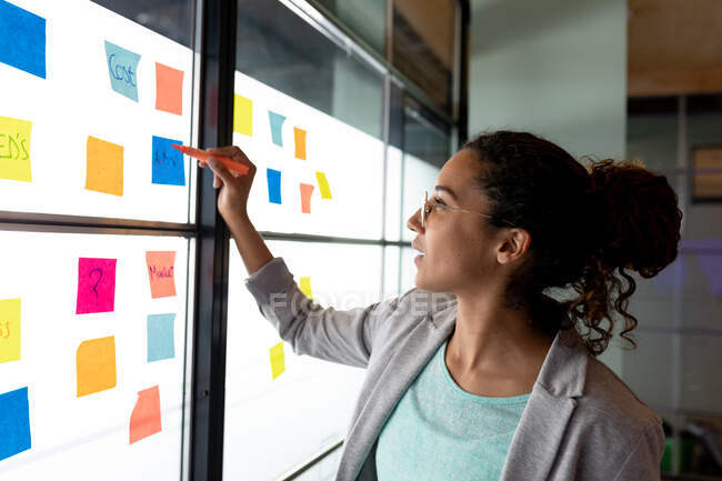 Biracial creative businesswoman planning strategy over sticky notes in office. creative business, modern office and business plan. — Stock Photo