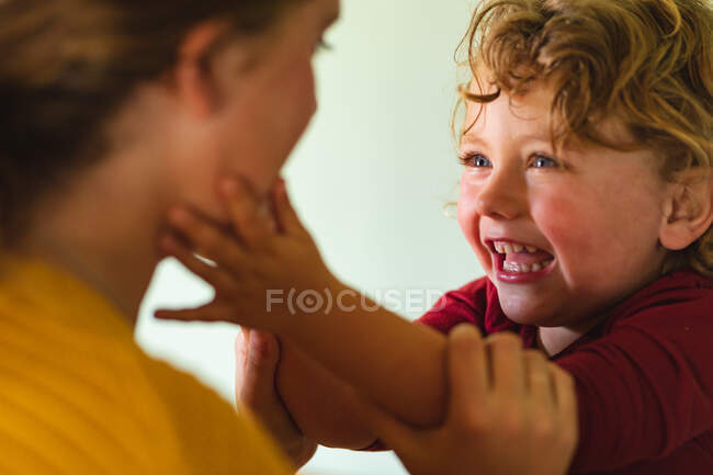 Sonriente chico rubio jugando mientras toca la mejilla de la madre en la cocina en casa. estilo de vida familiar, familiar y doméstico. - foto de stock