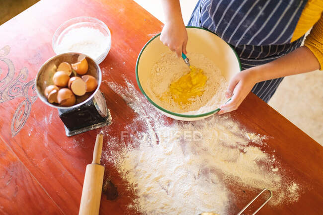 Midsection of woman mixing egg yolk and flour in bowl with spoon at table. domestic lifestyle and healthy eating. — Stock Photo