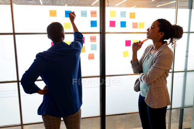 Многорасовые деловые женщины штурмуют разноцветные липкие ноты в креативном офисе. творческий бизнес, современный офис, мозговой штурм и бизнес-план. — стоковое фото