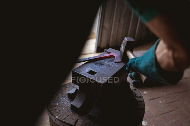 Image recadrée de forgeron dans des gants de protection forgeant avec un marteau sur enclume dans l'industrie. forgeage, métallurgie et industrie manufacturière. — Photo de stock