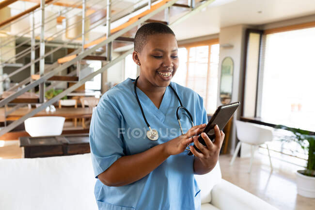Glückliche afrikanisch-amerikanische Ärztin in blauem Peeling mit digitalem Tablet im Krankenhaus. Gesundheitsdienstleistungen und drahtlose Technologie. — Stockfoto