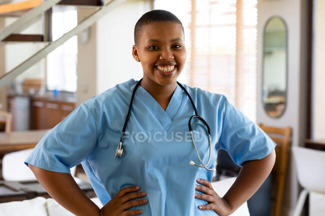Portrait of smiling african american female doctor in scrubs standing with arms akimbo in hospital. healthcare services. — Stock Photo