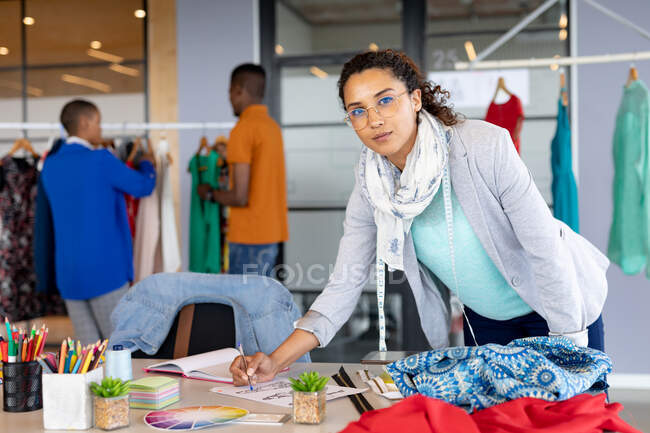 Retrato de designer de moda feminina biracial confiante em casuals trabalhando em design no escritório. negócio de design criativo, escritório moderno e moda. — Fotografia de Stock