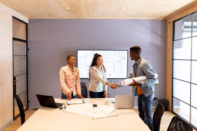 Male architect in casuals holding blueprint while handshaking with female colleague in office. creative design business, architect and office workplace. — Stock Photo