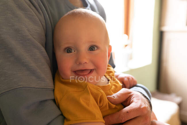 Midsection de jovem pai segurando bonito adorável sorrindo bebê em casa. estilo de vida familiar e doméstico. — Fotografia de Stock