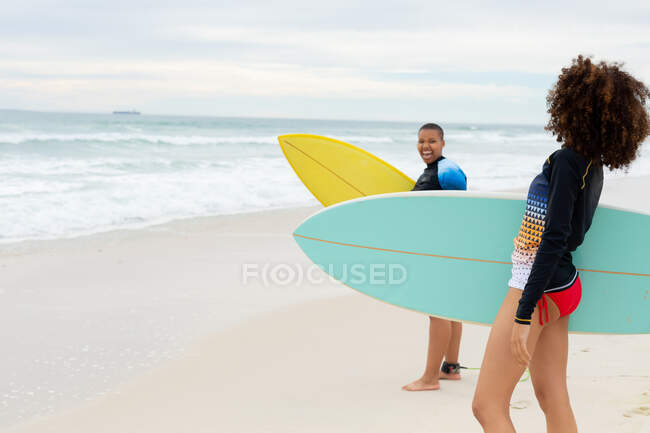 Мультирасовые подруги с досками для серфинга на берегу на пляже в выходные. дружба, серфинг и досуг. — стоковое фото
