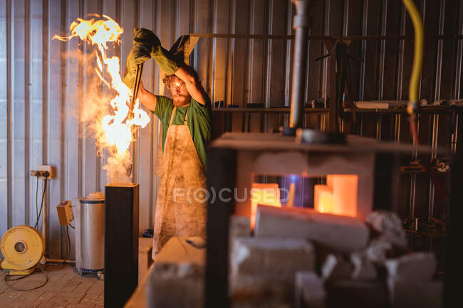 Ferreiro caucasiano colocando metal em fogo enquanto forja na indústria de fabricação. indústria de forjamento, metalurgia e indústria transformadora. — Fotografia de Stock