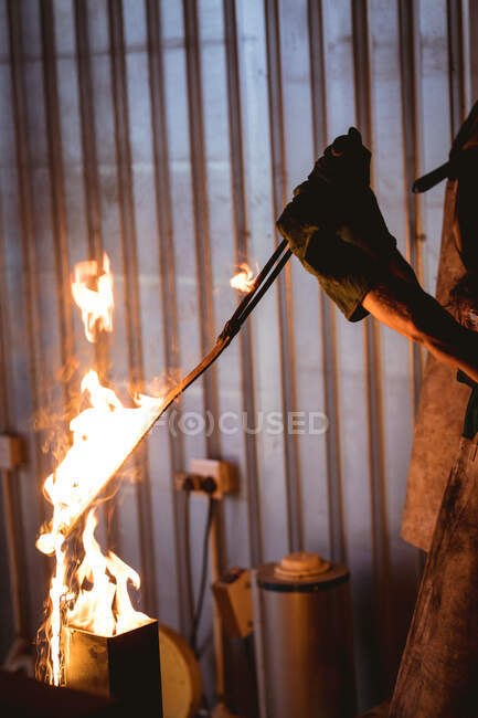 Cropped hands of blacksmith putting metal in fire while forging at manufacturing industry. forging, metalwork and manufacturing industry. — Stock Photo