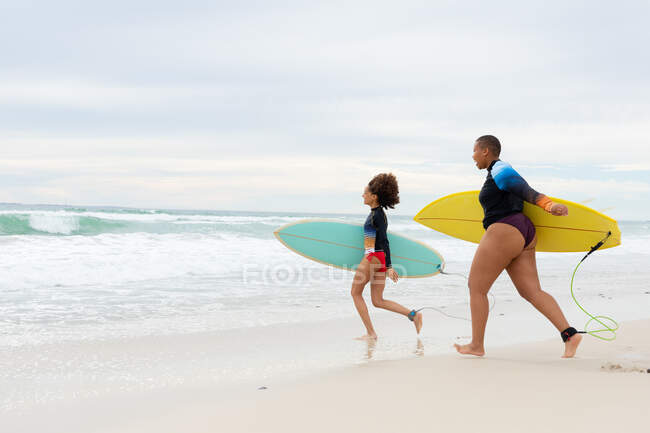 Full length of carefree multiracial female friends with surfboards running at beach during weekend. friendship, surfing and leisure time. — Stock Photo