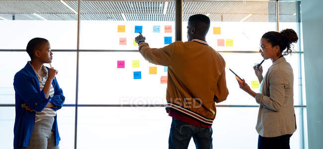 Multiracial male and female colleagues in smart casuals discussing over sticky notes in office. creative business, modern office, brainstorming and business plan. — Stock Photo