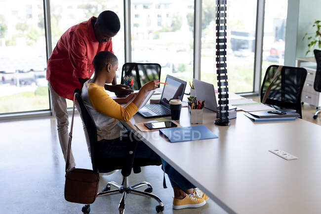 Des collègues d'affaires afro-américains dans des discussions informelles sur ordinateur portable dans un bureau créatif. entreprise créative, bureau moderne et technologie sans fil. — Photo de stock