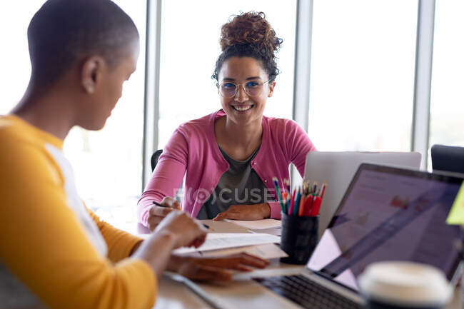 Mujer de negocios sonriente y colega en casualidades discutiendo sobre el documento en la oficina creativa. negocios creativos y negocios modernos. - foto de stock