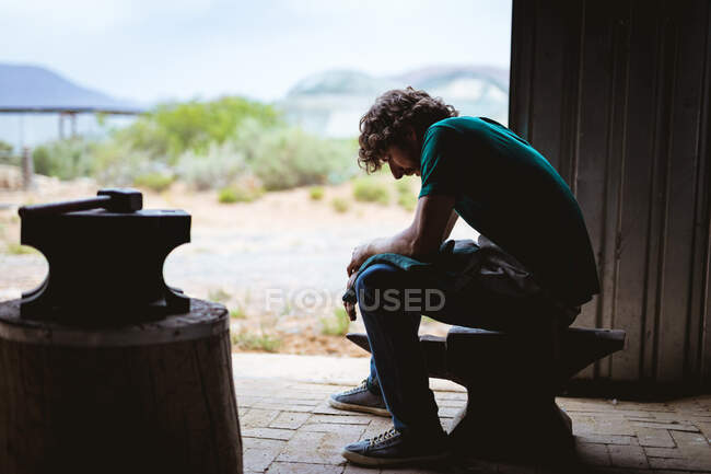 Seitenansicht von Schmied, der in der Metallindustrie auf einem Amboss sitzt. Schmiede-, Metall- und Fertigungsindustrie. — Stockfoto