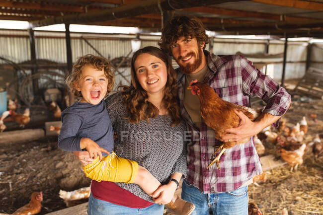 Портрет щасливої сім'ї, що стоїть з куркою на пташиній ручці в органічній фермі. осідання та птахівництво, тваринництво та сім'я . — стокове фото