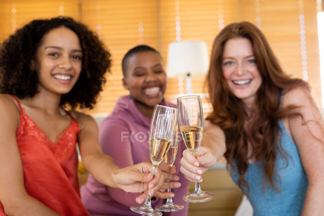 Felices amigas multirraciales brindando flautas de champán durante la fiesta de la casa. amistad, socialización y tiempo libre. - foto de stock
