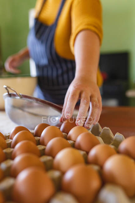Midsection of woman with flour on fingers picking brown egg from carton in kitchen. domestic lifestyle and healthy eating. — Stock Photo