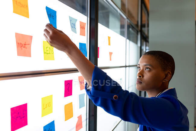 African american creative businesswoman in casual planning strategy over sticky notes in office. entreprise créative, bureau moderne et plan d'affaires. — Photo de stock