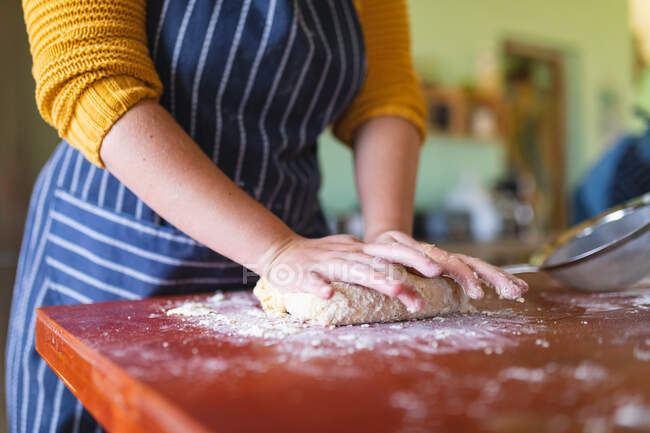 Midsection of woman wearing apron kneading dough on wooden table in kitchen at home. domestic lifestyle and healthy eating. — Stock Photo