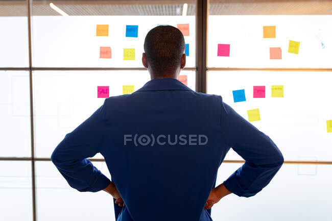 Rear view of businesswoman standing with arms akimbo in front of sticky notes at creative office. creative business, modern office, brainstorming and business plan. — Stock Photo
