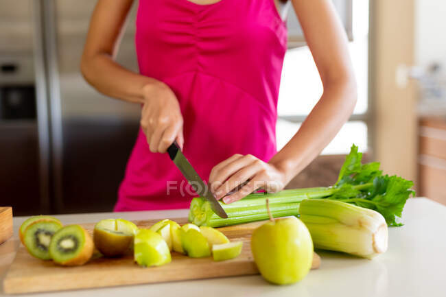 Midsection of woman in casual chopping vegetable by avocados on kitchen island at home. socialising, food and house party. — Stock Photo