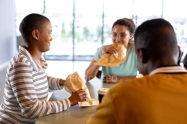 Multiracial male and female colleagues in casuals eating snacks at table during break in office. creative business and modern office. — Stock Photo