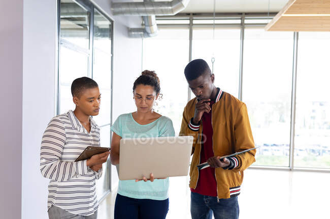 Multiracial male and female colleagues in casuals discussing over laptop in creative office. creative business, modern office and wireless technology. — Stock Photo