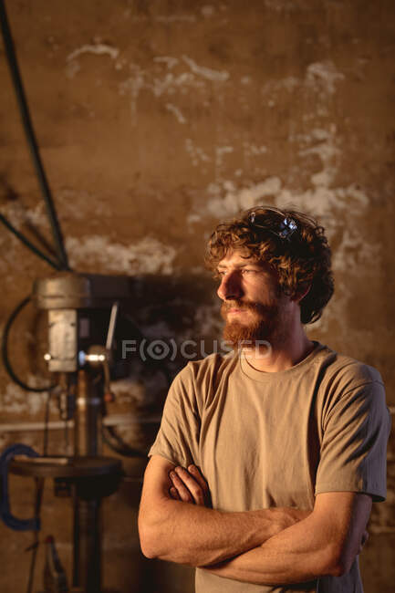 Thoughtful bearded caucasian blacksmith looking away while standing with arms crossed in industry. forging, metalwork and manufacturing industry. — Stock Photo