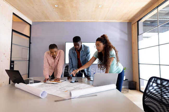 Multiracial male and female architects in casuals discussing over blueprint at conference table. creative design business, architect and office workplace. — Stock Photo